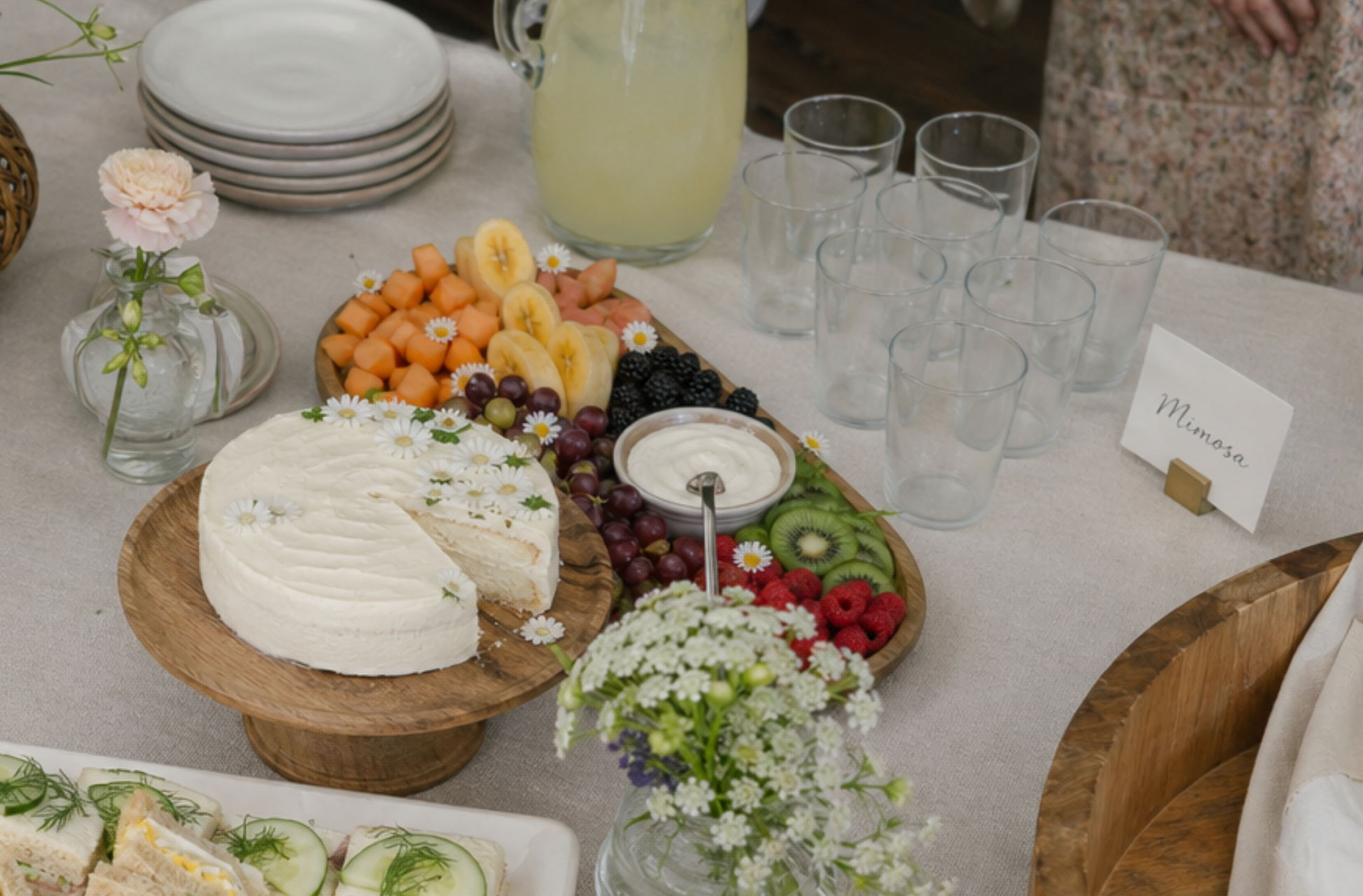 baby shower brunch spread flat lay with finger sandwiches fruit tray cake and lemonade on neutral linen